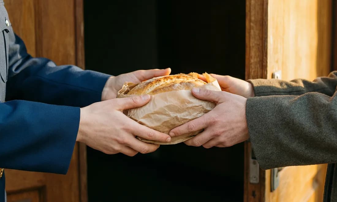 A paper-wrapped loaf passing between two pairs of hands in a doorway.